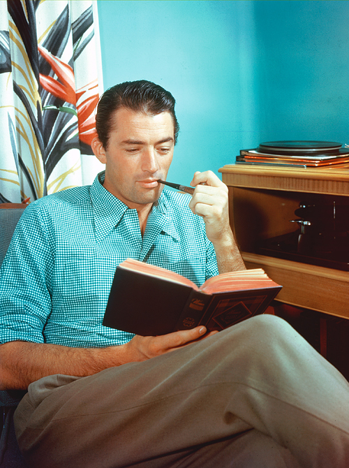 Gregory Peck (1916-2003), US actor, smoking a pipe while reading a book, while listening to records playing on a turntable beside him, circa 1955. (Photo by Silver Screen Collection/Getty Images)